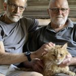 Donald Currie and Daniel Gladstone sitting both in grey shirts with their orange cat on their laps