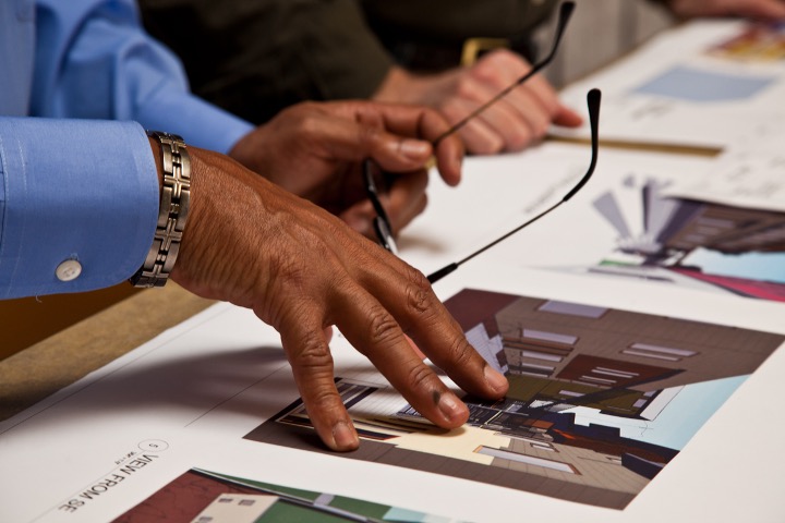 Hands holding glasses in one and pointing to a picture on the table with the other